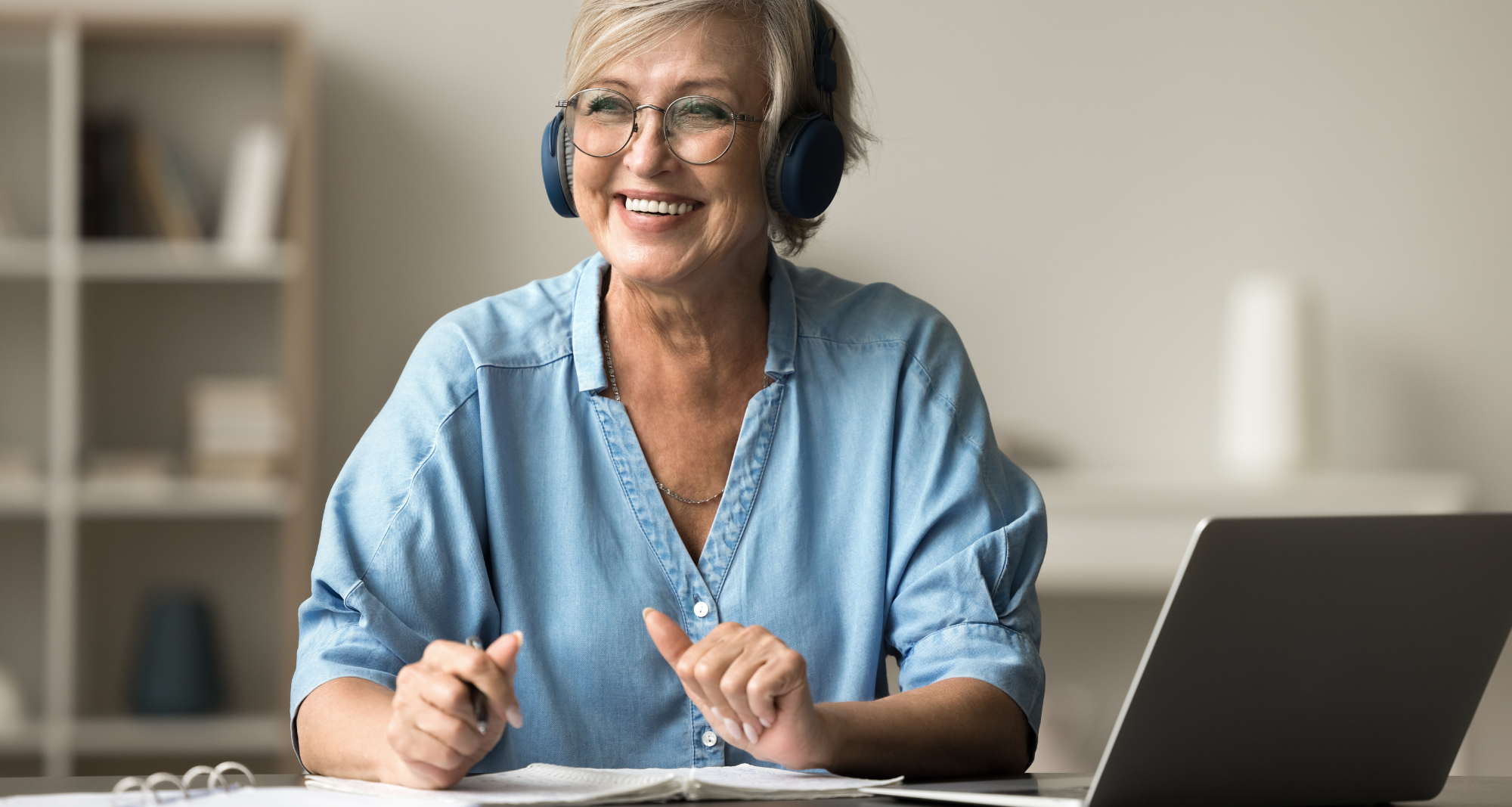 Une femme âgée heureuse s'assoit au bureau avec un ordinateur portable.